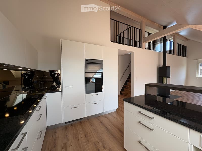 Modern kitchen with white cabinets, black countertops, and stainless steel appliances. Open layout with a visible staircase leading to an upper level.