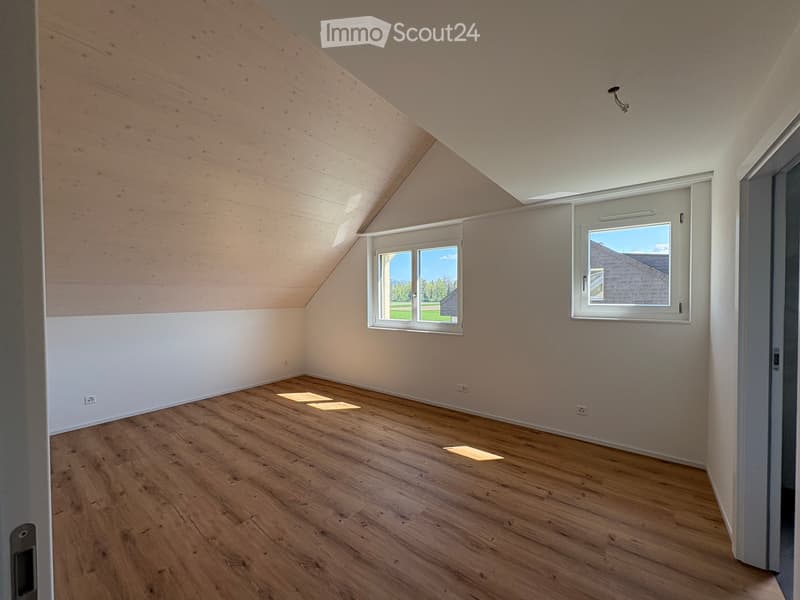 Empty attic room with wooden floors, white walls, and skylight windows, featuring exposed wooden beams on the ceiling.