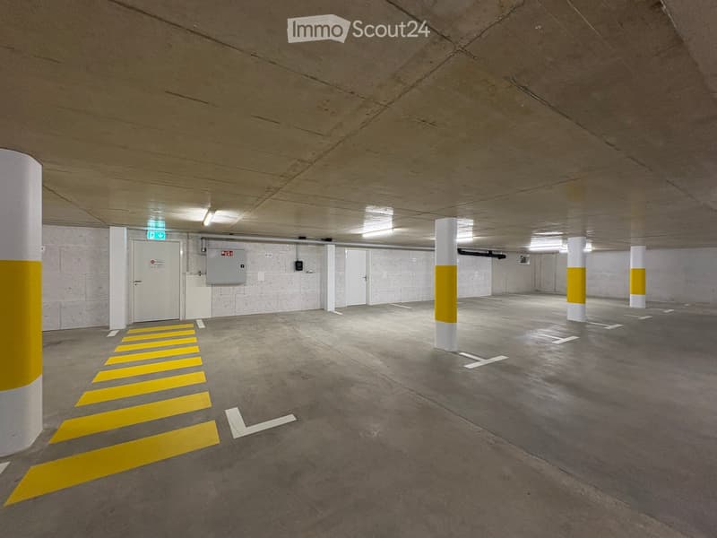 Underground parking area with concrete pillars, marked parking spaces, and emergency exit signage.