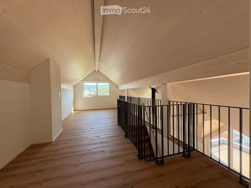 Spacious hallway with wooden flooring, modern black metal railing, and large windows offering a scenic view.