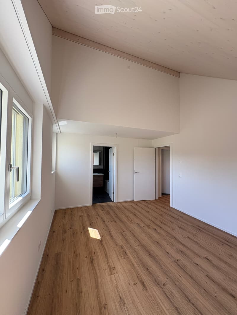 Empty room with wooden flooring, white walls, and large windows. Two doors lead to other rooms.