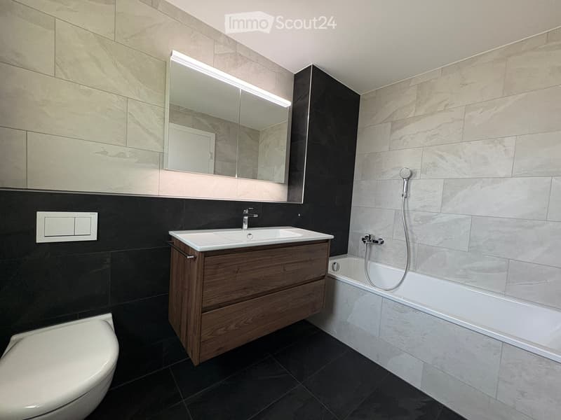 Modern bathroom with a wooden vanity, white sink, bathtub, toilet, and large mirror with LED lighting.