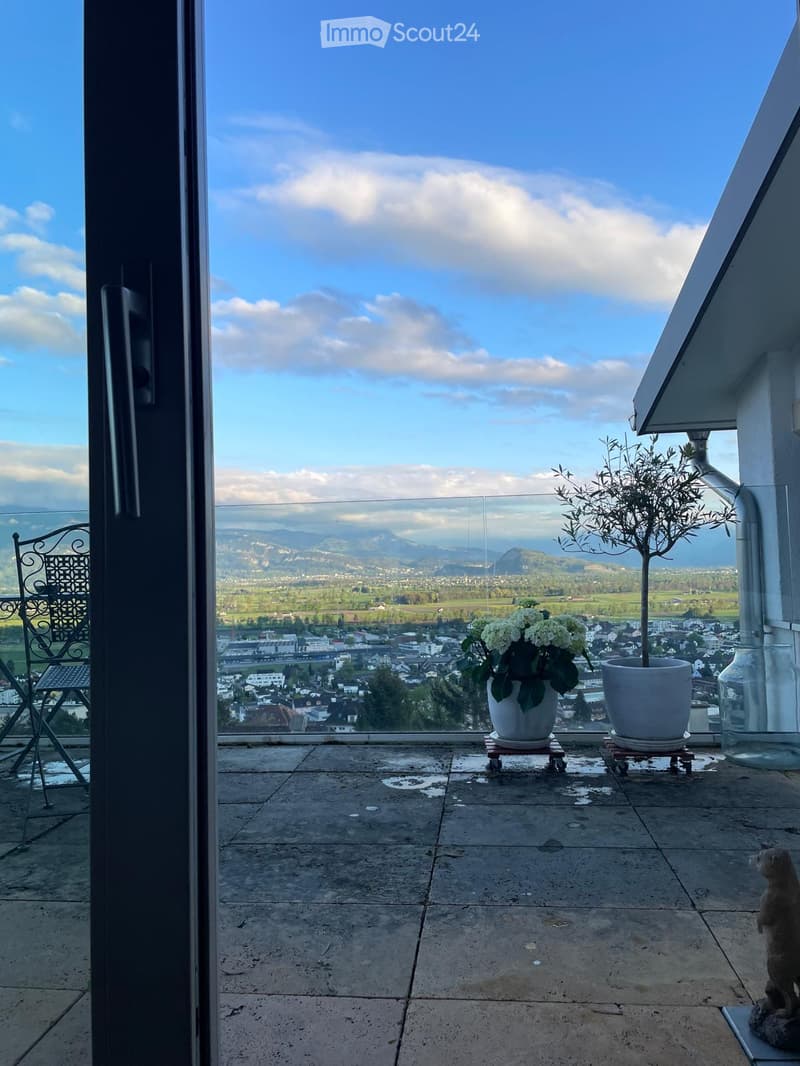 Balcony with a scenic view, featuring a metal chair, small table, potted plants, and a decorative glass vase.