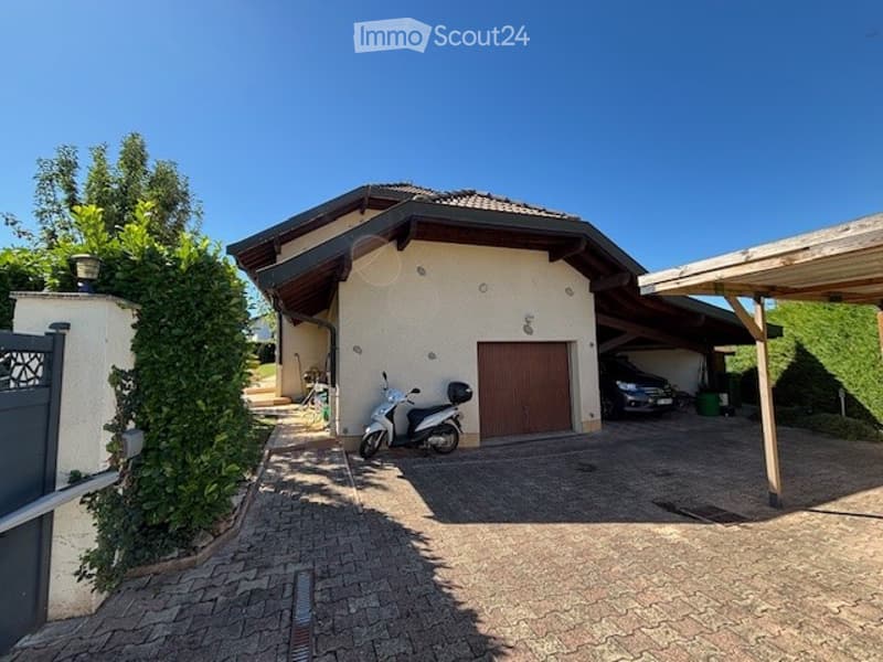 Two-story house with a garage, driveway, and covered parking area. The house has a modern design with a tiled roof and light-colored exterior walls.