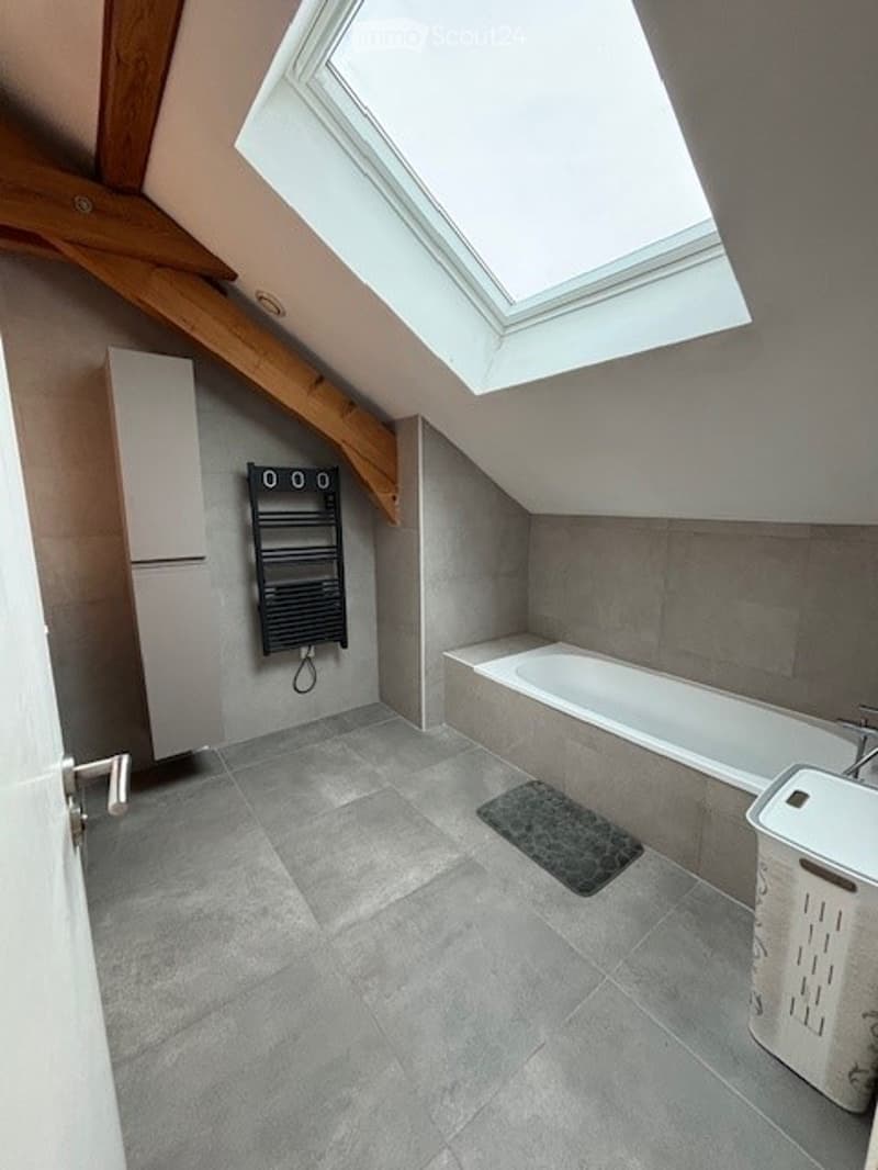 Modern bathroom with grey tiles, a bathtub, a sink, a radiator, and a built-in cabinet. Features a skylight window for natural light.