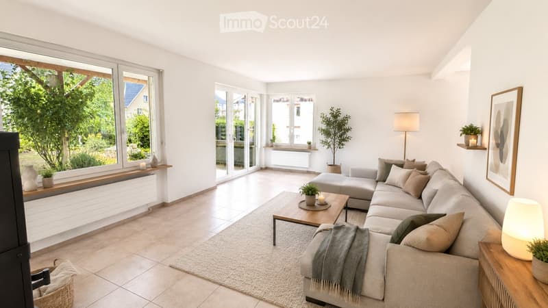 Bright living room with large windows, a sectional sofa, coffee table, floor lamp, and decorative plants.