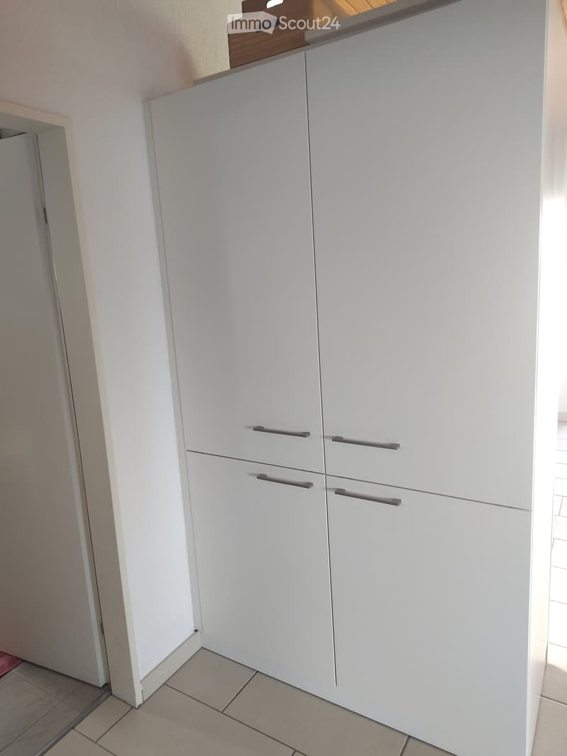 Modern kitchen with white cabinets and sleek handles, featuring a tiled floor and a visible doorway to another room.