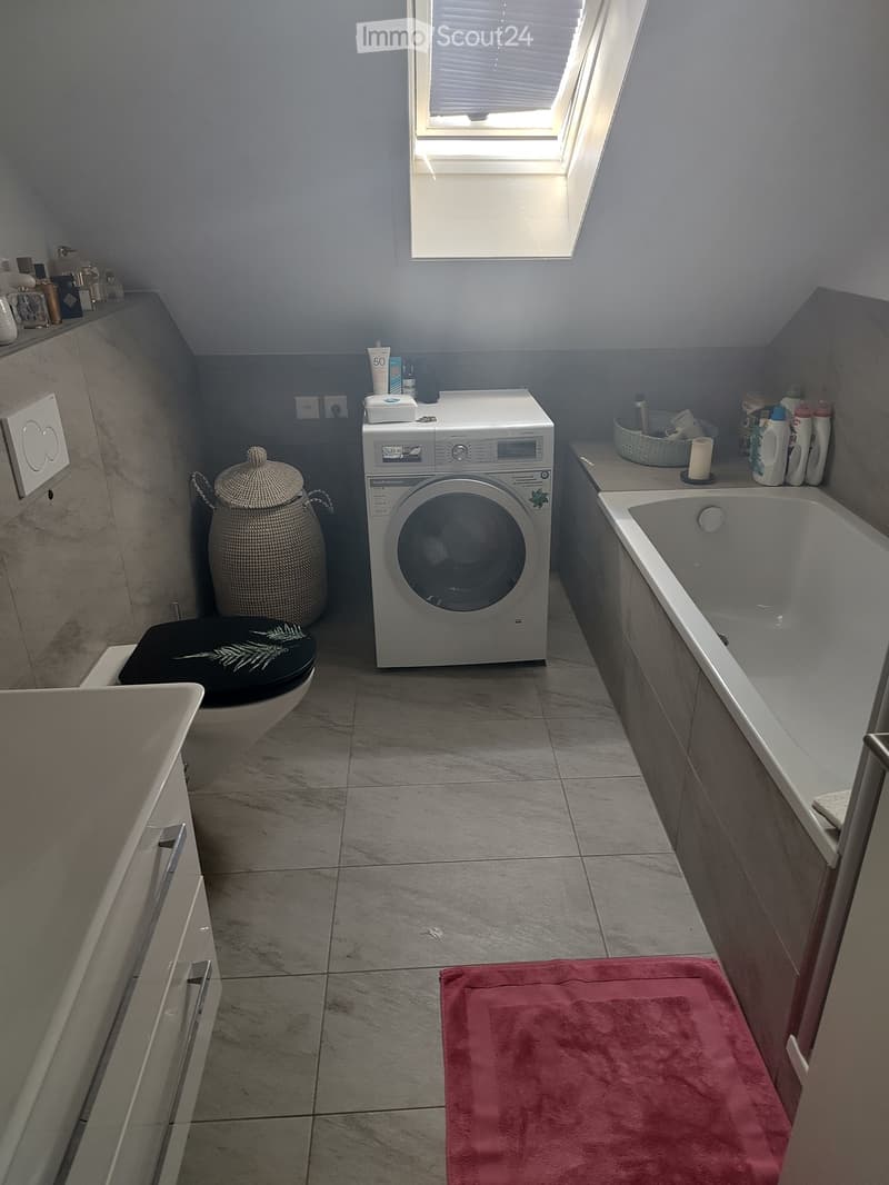 Bathroom with a toilet, bathtub, washing machine, wicker basket, and various toiletries and cleaning supplies.
