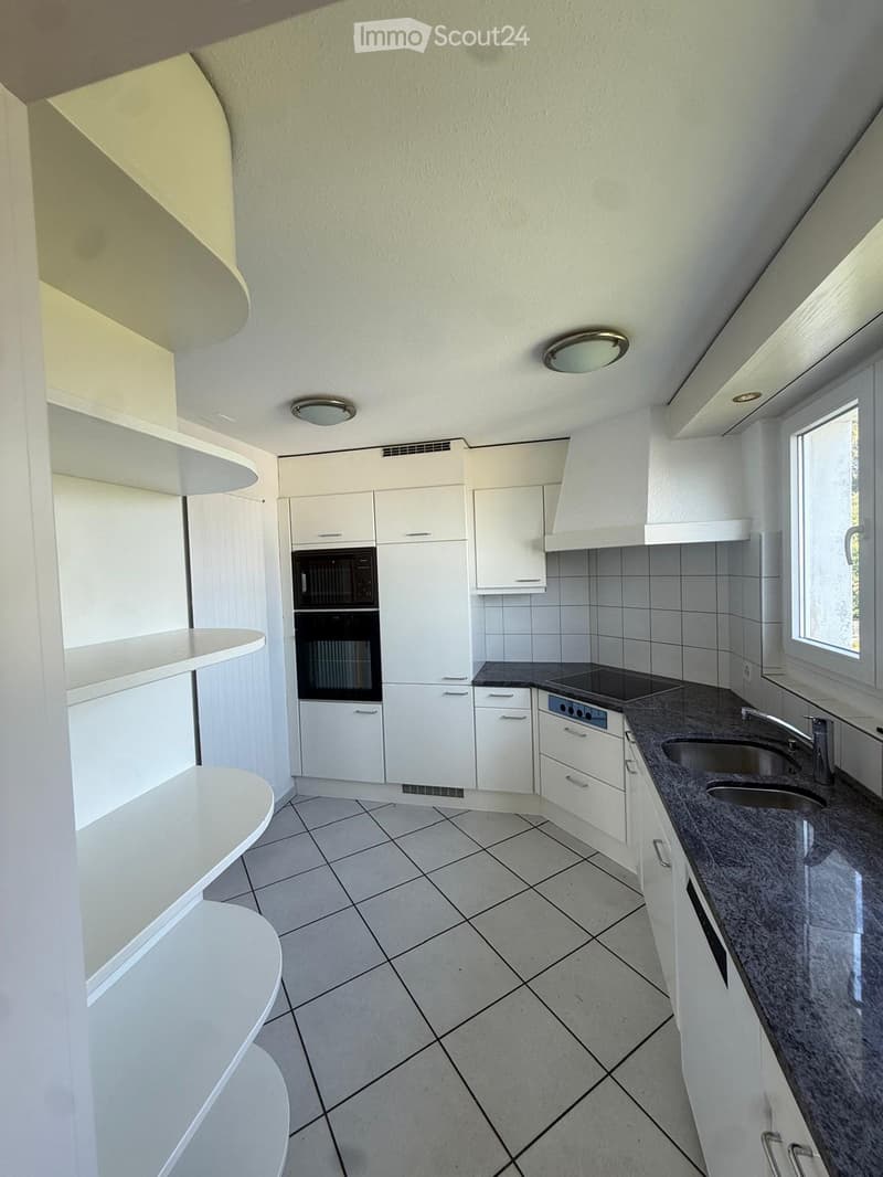 Modern kitchen with white cabinets, stainless steel appliances, and a dark countertop. Features include a sink with a faucet, an oven, microwave, and built-in storage.