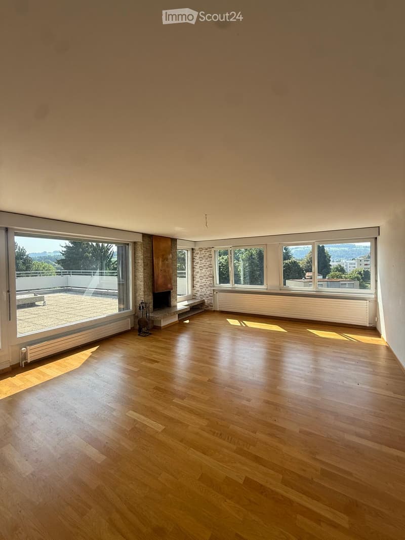 Empty room with wooden flooring, large windows, and a fireplace. No furniture or equipment present.