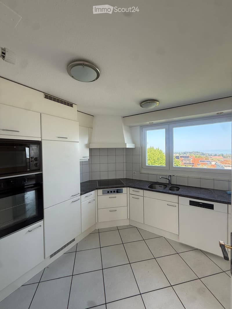 Modern kitchen with white cabinets, black countertop, built-in oven, sink, and large windows offering a scenic view.