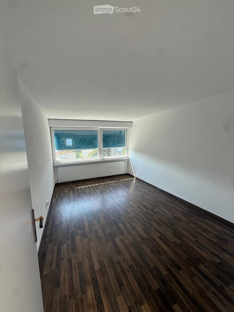 Empty room with wooden flooring, white walls, a window with blinds, and a radiator below the window.