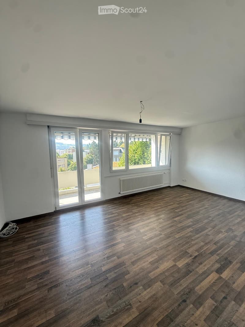 Empty room with wooden flooring, white walls, large windows, and a radiator. No furniture or equipment present.