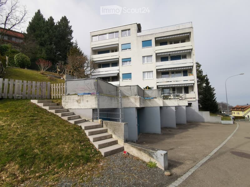 Multi-story apartment building with balconies, located on a raised ground floor with steps leading up to the entrance.