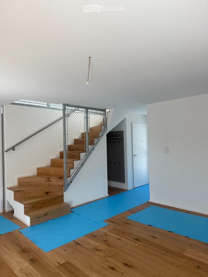 Bright hallway with wooden flooring, a staircase with wooden steps and metal railing, blue exercise mats on the floor, and a closet with white doors.