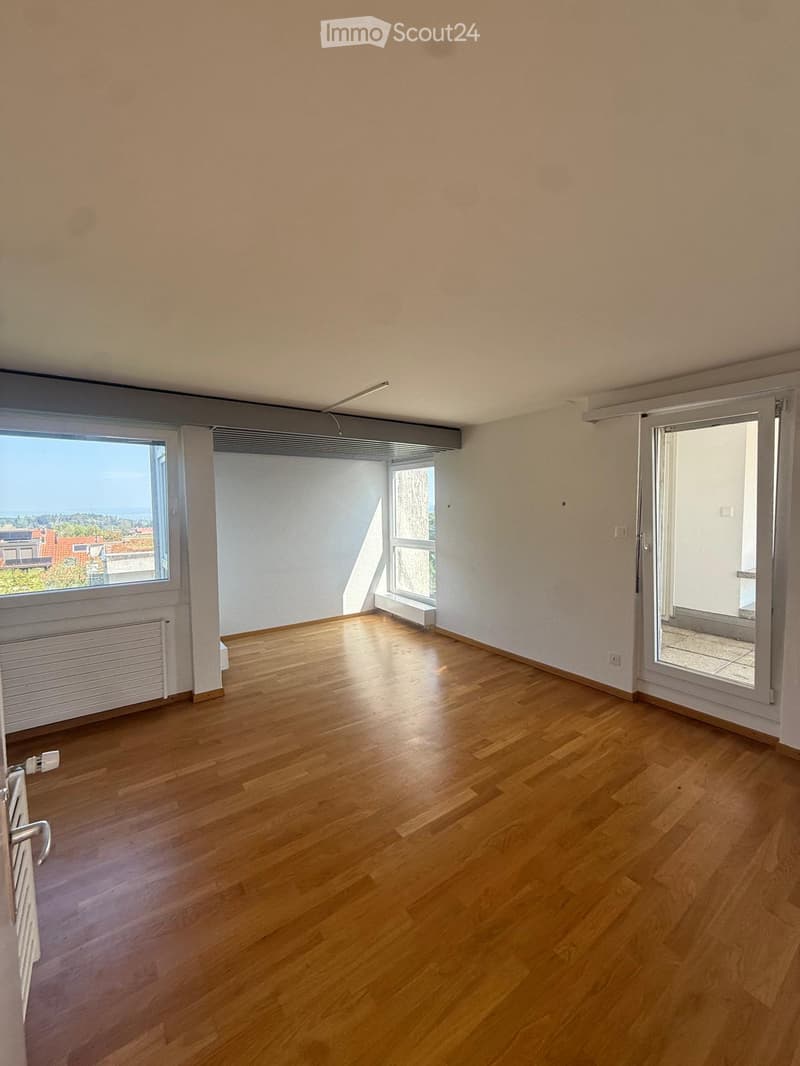 Empty room with wooden flooring, large windows, and a sliding glass door leading to a balcony.