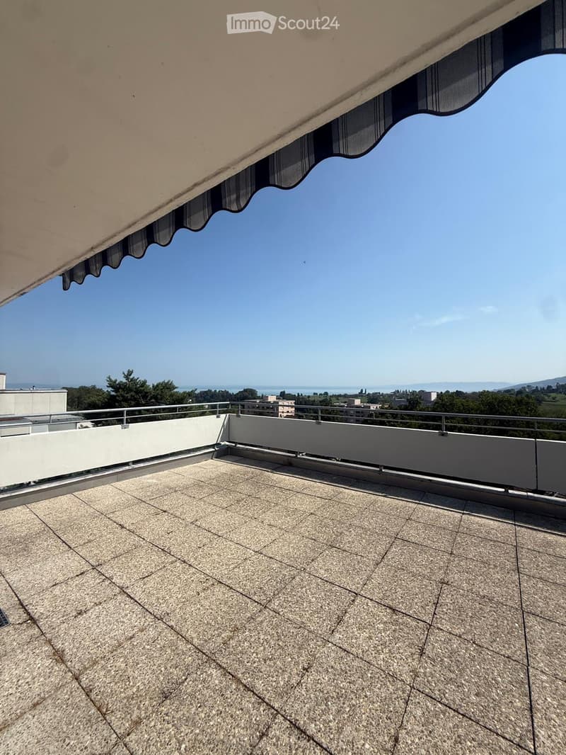 Roof terrace with tiled surface, metal railing, and scenic view of the sea and distant landscape.