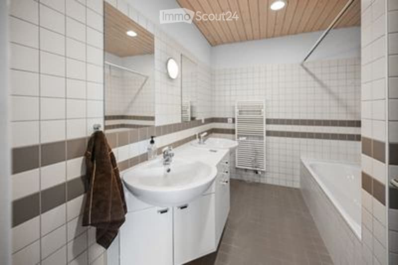 Modern bathroom with white tiles, a double sink vanity, a bathtub, a towel hanging on the wall, and a radiator.