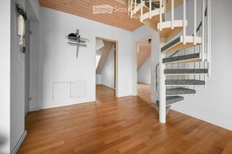 Bright, unfurnished room with wooden flooring and white walls. Features a spiral staircase leading to an upper level and a coat rack on the wall.