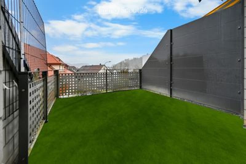 Small, enclosed patio with artificial grass, surrounded by metal fencing and a gray wall.