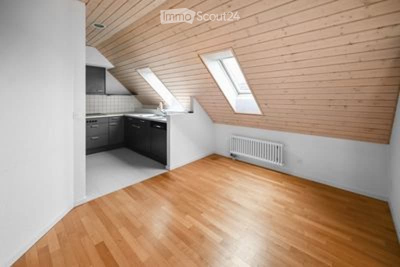 Bright, open-plan room with wooden flooring, white walls, and skylight windows. Kitchen area with cabinets and sink visible.