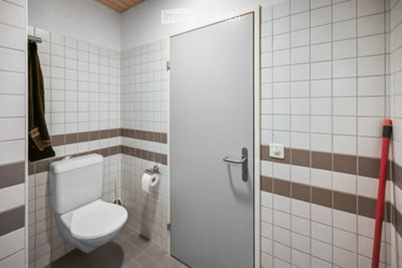 Modern bathroom with white tiled walls, a toilet, a door, and a toilet paper holder. The walls feature brown and white tiles, and a towel hangs on the left side.