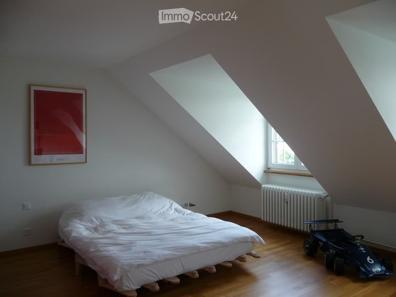 Bright attic bedroom with wooden flooring, a single bed, a toy car, a radiator, and a framed picture on the wall.
