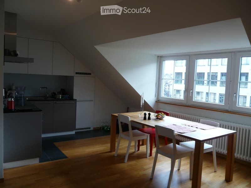 Bright, modern kitchen and dining area with wooden flooring, large windows, a dining table with chairs, and a kitchen area with cabinets and a sink.