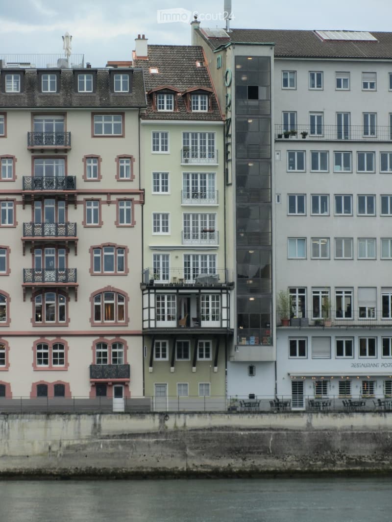 Row of multi-story buildings with balconies, large windows, and varied facades, situated along a waterfront.