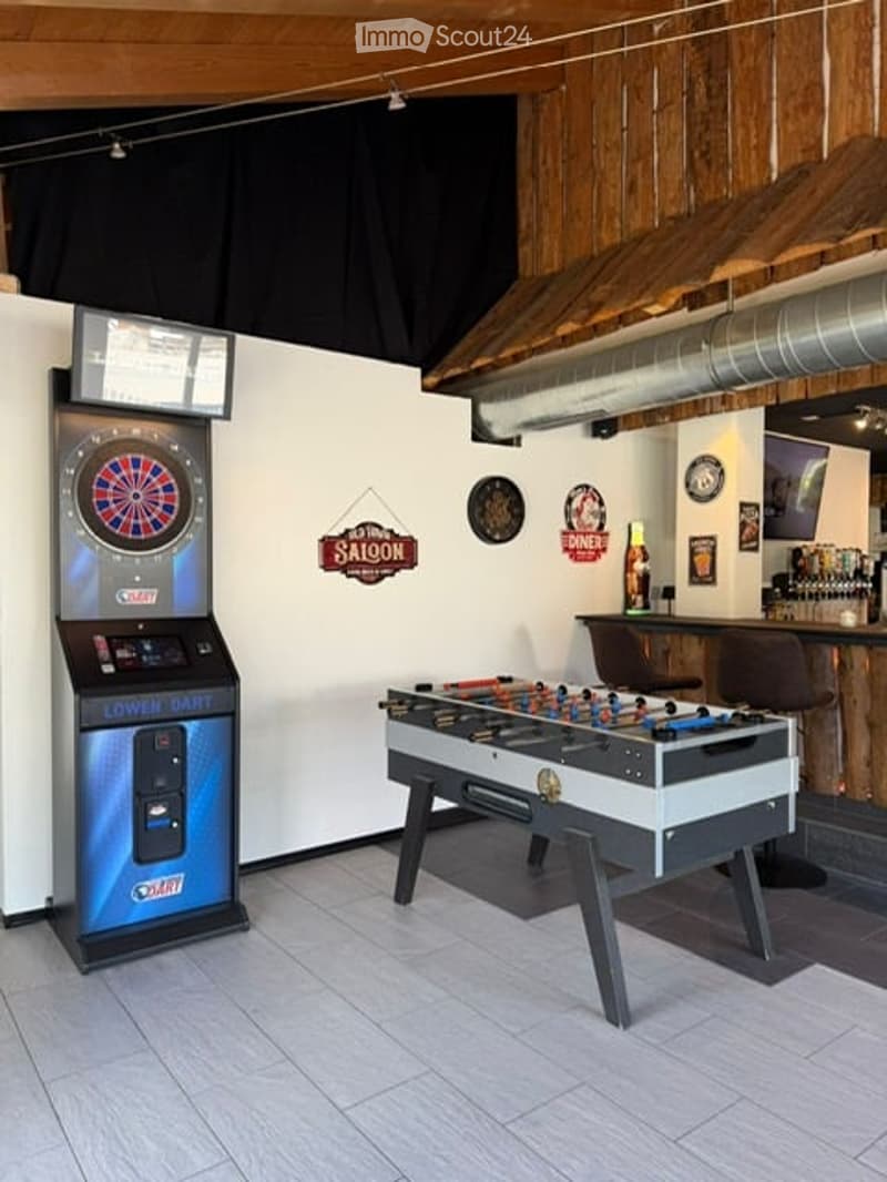 A recreational room with a dartboard machine, foosball table, bar counter, and various decorations including signs and picture frames.