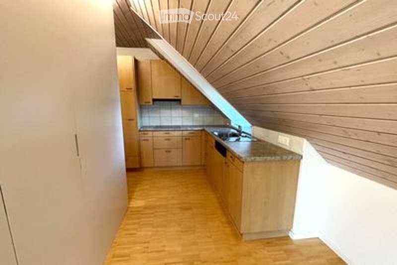 Bright kitchen with wooden cabinets, a sink, and a granite countertop, featuring a slanted wooden ceiling and light wooden flooring.