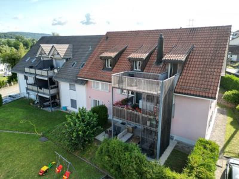 Aerial view of a multi-unit residential building with a red-tiled roof, balconies, and surrounding greenery.
