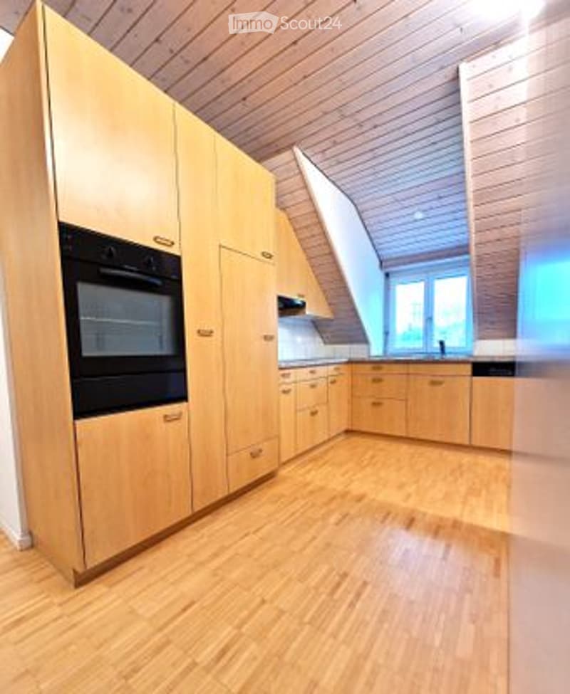 Modern kitchen with light wood cabinetry, an oven, and a sink, featuring a clean and organized design with a wooden floor.
