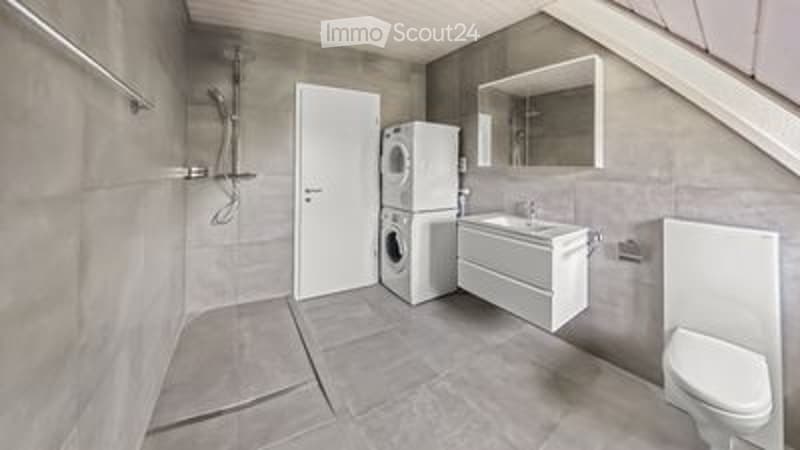 Modern bathroom with grey tiles, white fixtures, a toilet, sink, mirror, and a washing machine.