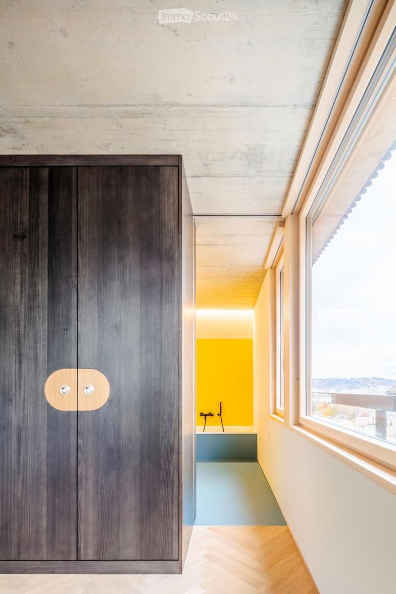 Modern hallway with wooden flooring, grey built-in wardrobe, and a view into a brightly lit bathroom with yellow walls and blue floor.