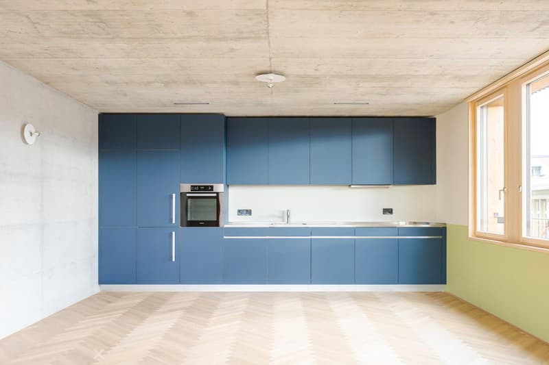 Modern kitchen with blue cabinets, stainless steel oven, and wooden flooring.