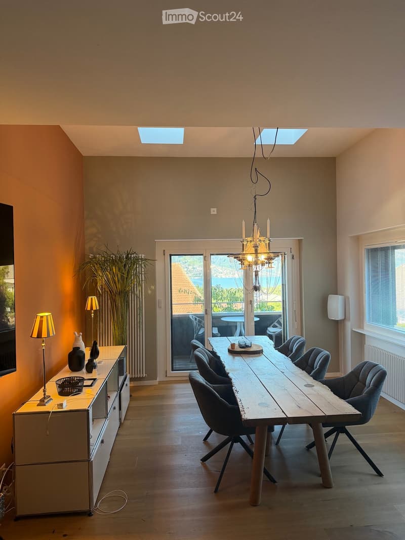 Bright kitchen with wooden dining table, modern chairs, cabinet, and decorative vases. Large windows and a view of the outdoor area.