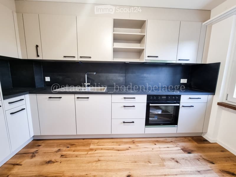 Modern kitchen with white cabinets, black countertops, wooden flooring, sink, faucet, and oven.