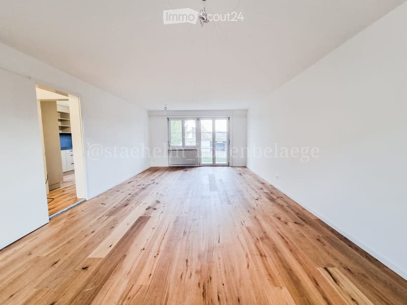 Empty room with wooden flooring, white walls, and large glass doors leading to a balcony.