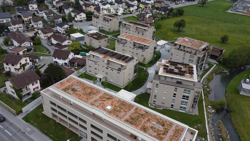 Aerial view of a residential area with multiple apartment buildings, green spaces, and a small stream running through the neighborhood.