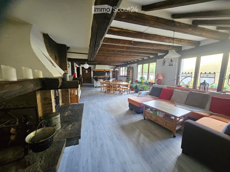 Open-concept living and dining area with exposed wooden beams, a stone fireplace, a sofa, coffee table, dining table, and chairs.