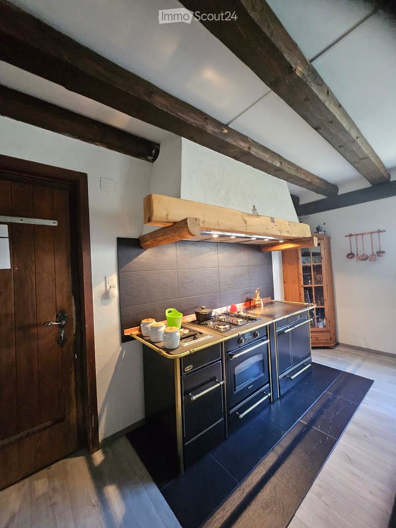Modern kitchen with stainless steel appliances, wooden beams, and a dark tiled floor.