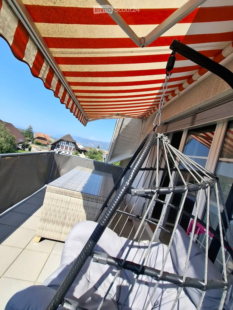 Balcony with a hanging egg chair, striped awning, and scenic mountain view in the background.
