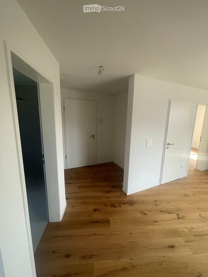 Empty hallway with light wooden flooring, white walls, and several closed doors leading to other rooms.