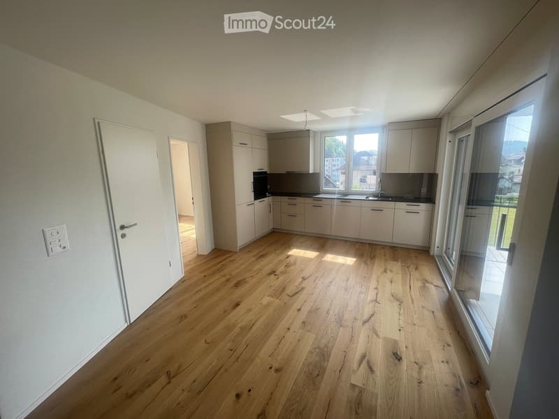 Empty kitchen with light wooden flooring, white cabinets, and large windows offering a view of the outside. No furniture or appliances are present.