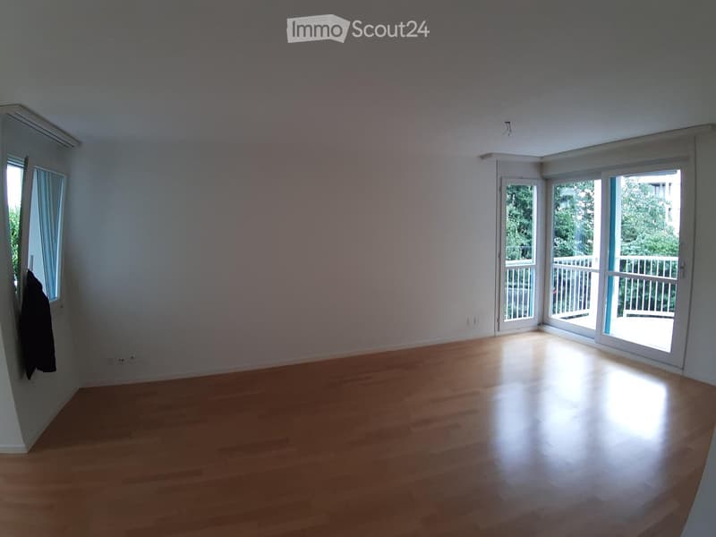 Empty room with wooden flooring, white walls, large windows, and sliding glass doors leading to a balcony.