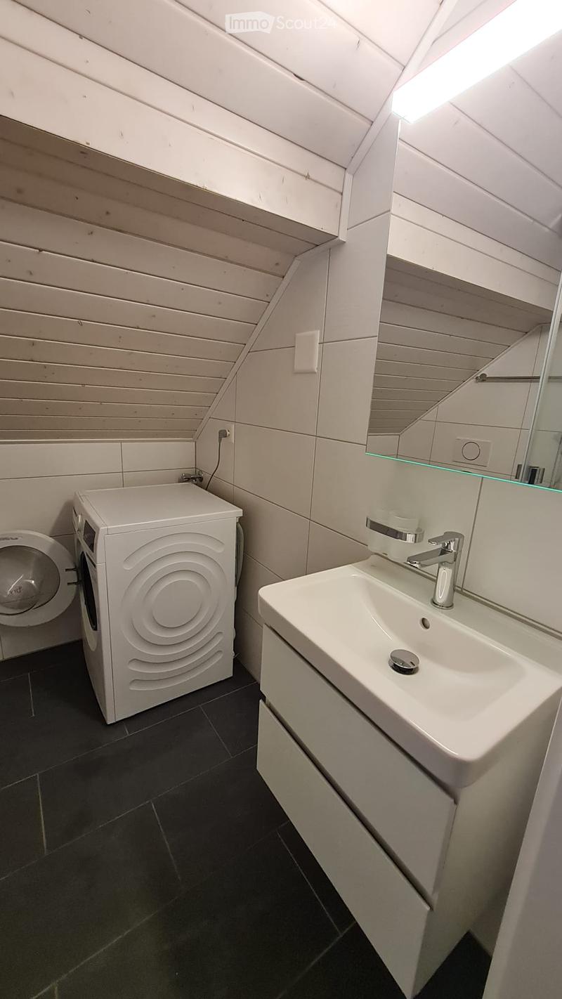 Small bathroom with white tiles, a toilet, a washing machine, a sink, and a mirror.