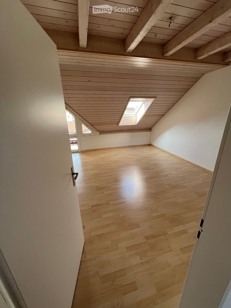Empty attic space with wooden floors and slanted wooden ceilings, featuring skylight windows and exposed wooden beams.