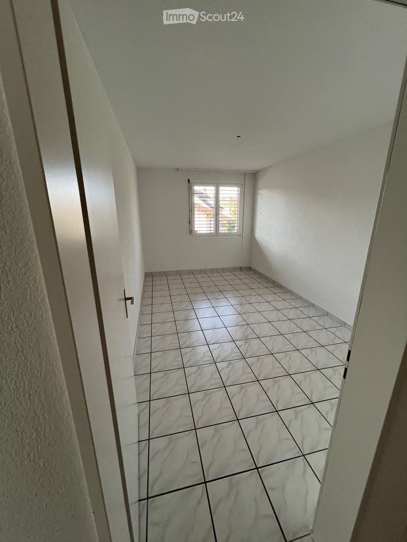Empty hallway with tiled floor and white walls, featuring a small window at the far end.