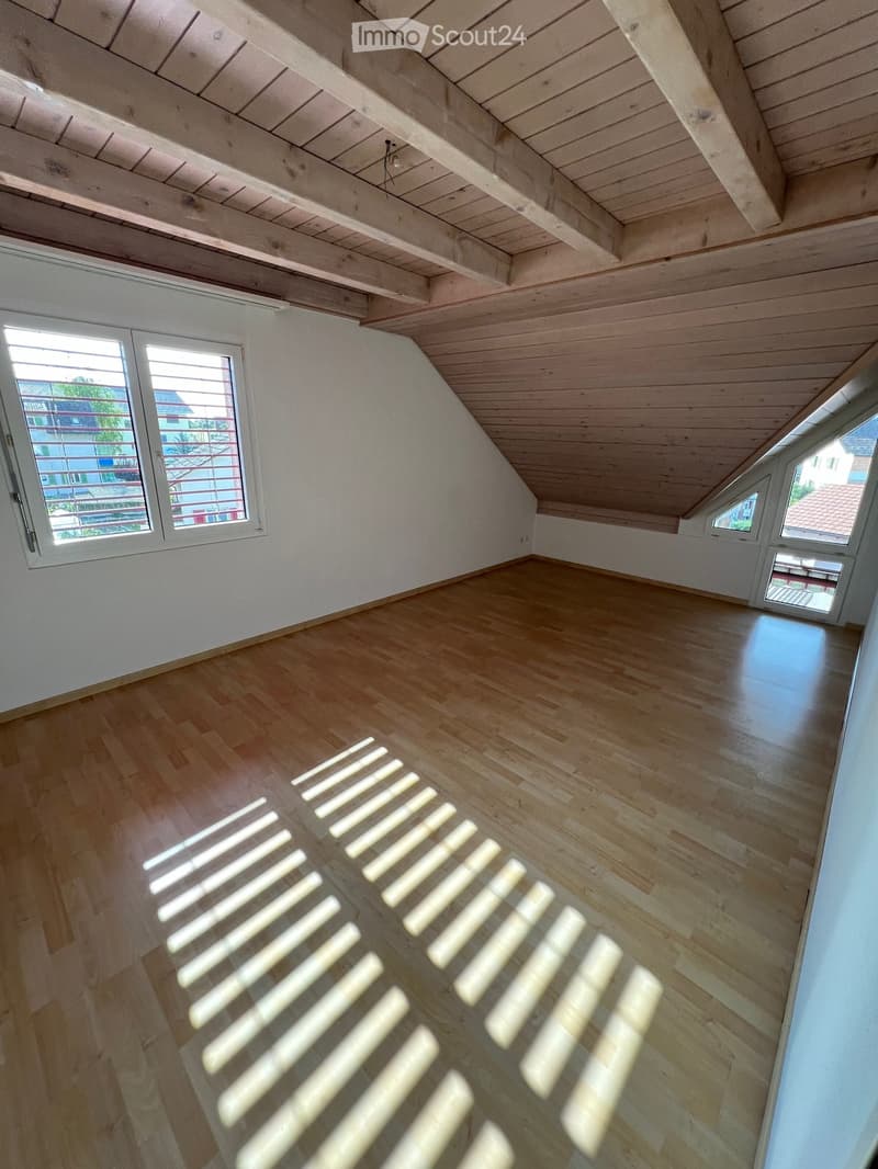 Empty attic room with wooden floor and slanted wooden ceiling, featuring multiple windows allowing natural light to enter.